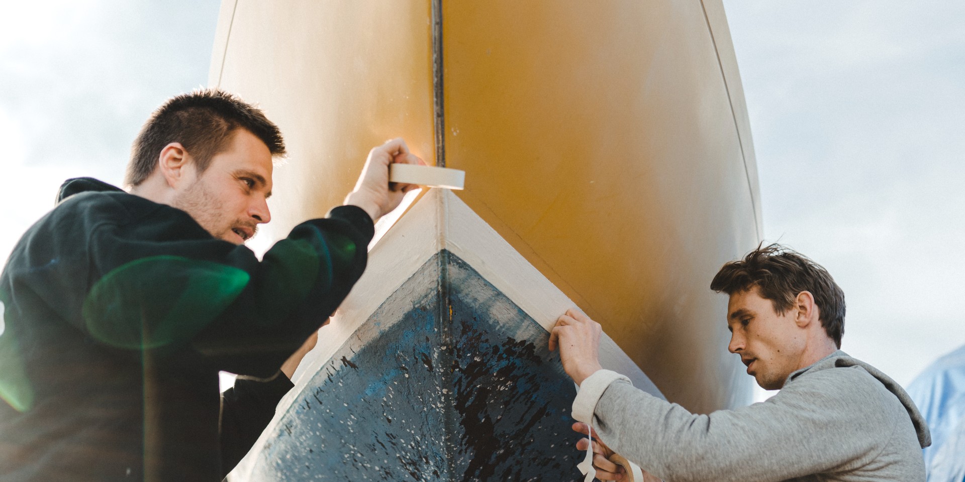 Två män sätter dit maskeringstejp på båtskrovet