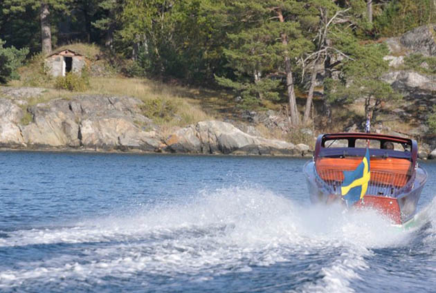 Röd båt med svenska flaggan som åker på sjön