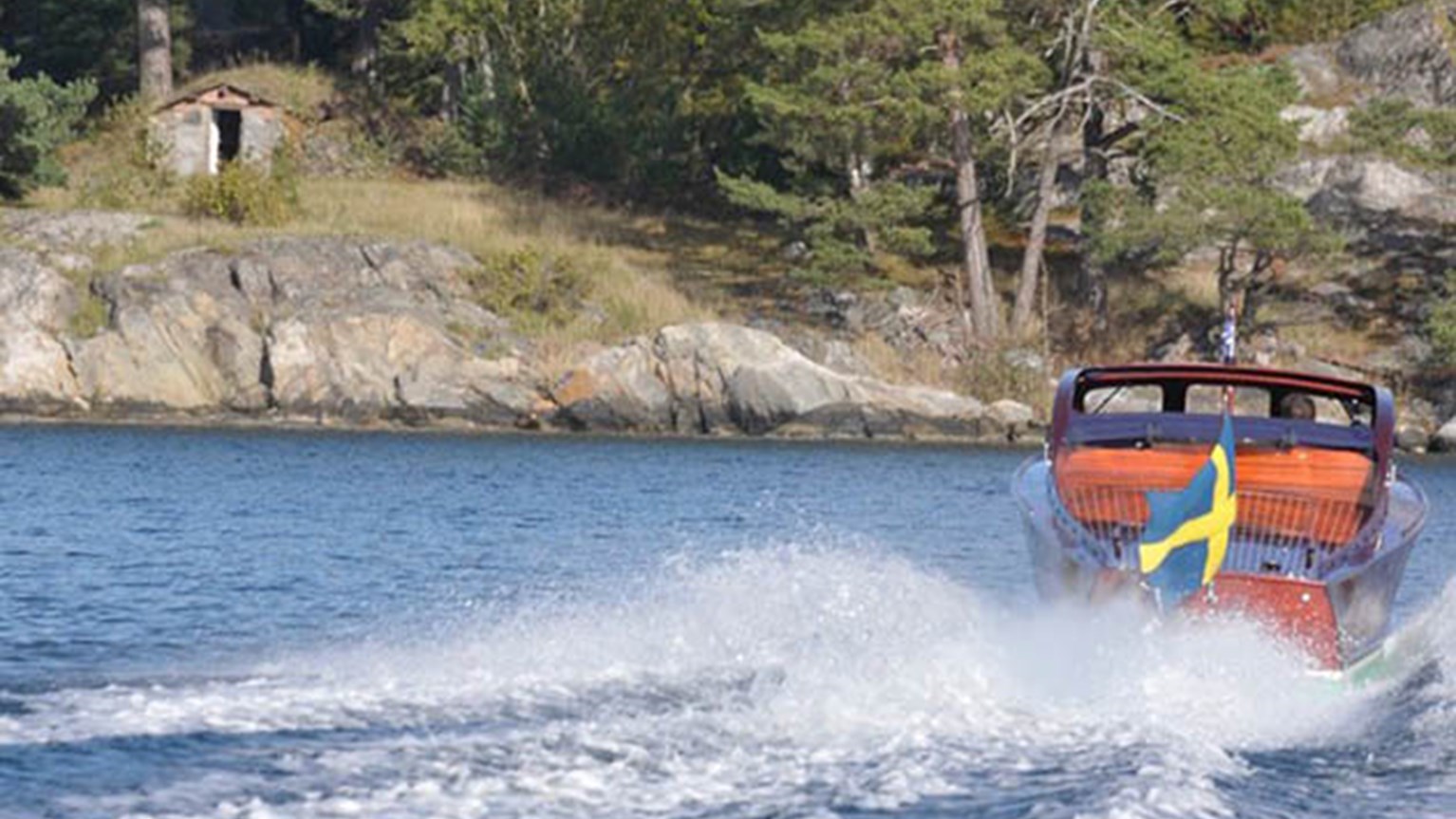 Röd båt med svenska flaggan som åker på sjön